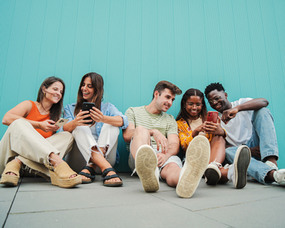 group of diverse friends smiling and cheerfully looking on phones