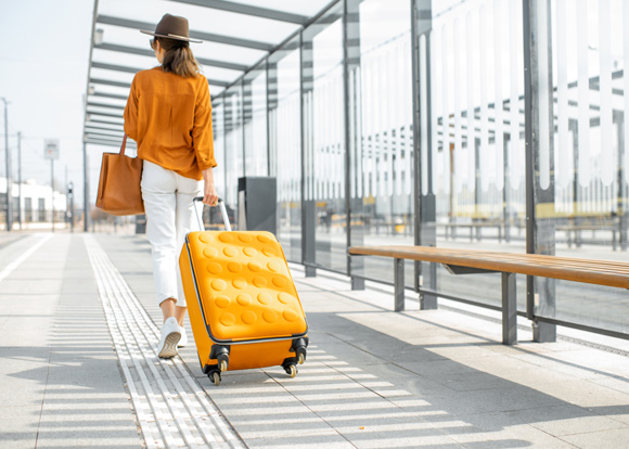 woman pulling yellow suitcase along pathway in yellow shirt and brown fedora hat
